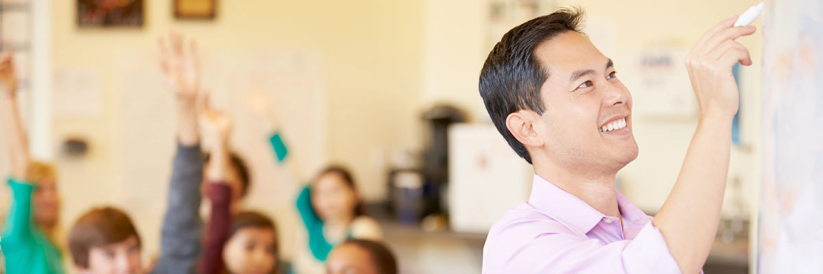 Teacher in front of his class writing on chalkboard